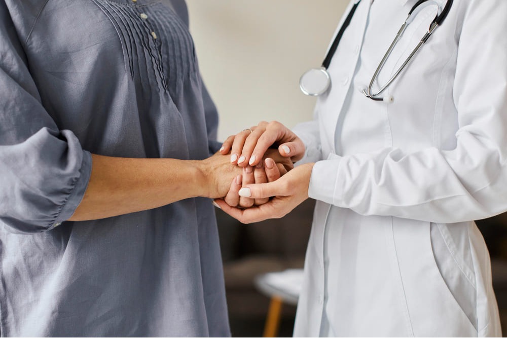 Médica segurando as mãos de paciente